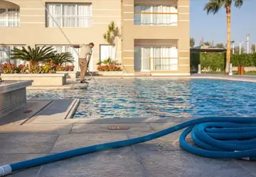Man cleaning a pool with pool vacuum hose coiled on pool deck
